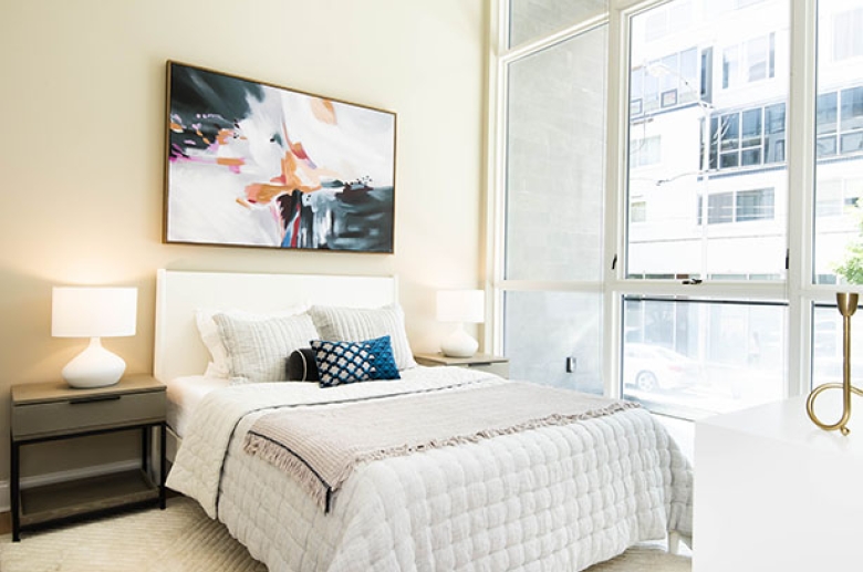 A furnished bedroom with glass windows across the entire right wall with an adjacent balcony.