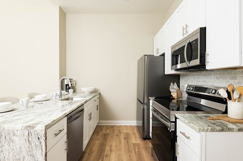 A kitchen aisle with a sink across from the cabinets, a refrigerator, a stove, and a microwave