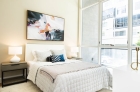 A furnished bedroom with glass windows across the entire right wall with an adjacent balcony.