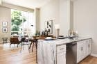 A kitchen aisle with a sink, a dishwasher, and cabinets, with a view of the adjacent living room in the background.  