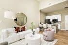 A furnished living room with an adjacent dining area on the kitchen aisle and a furnished kitchen in the background.